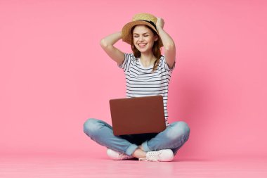 Dizüstü bilgisayarı olan bir kadın internet alışverişinde pembe arka planda oturuyor.