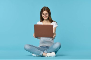 Dizüstü bilgisayarı olan kadın yerde oturuyor ve mavi arka planda öğrenci teknolojisi öğreniyor.