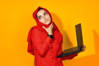 Elinde dizüstü bilgisayarla kırmızı tesettürlü kadın. Teknoloji, duygu, etnik model.