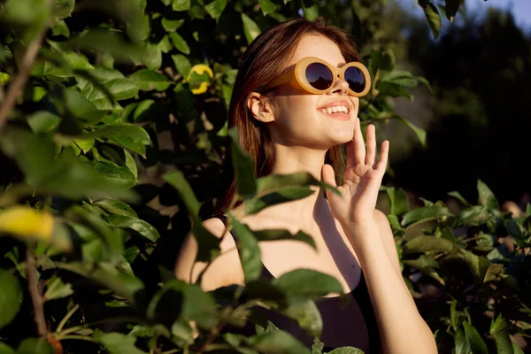 Wesoła kobieta nosi okulary przeciwsłoneczne zielony liście natura lato pozowanie — Zdjęcie stockowe