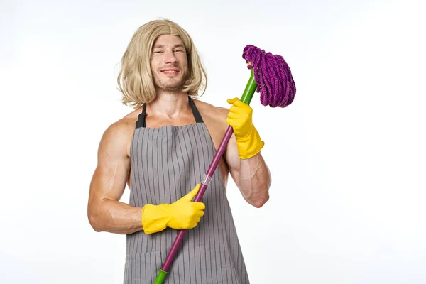 Muscular man in apron with a mop in a womans wig — Stock Photo, Image