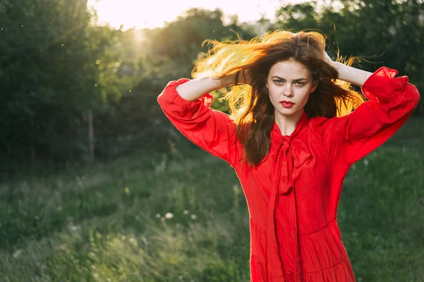 Attraktiv kvinna i röd klänning poserar i naturen grönt gräs — Stockfoto