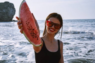 Ellerinde karpuz olan siyah mayo giymiş güzel bir kadın.