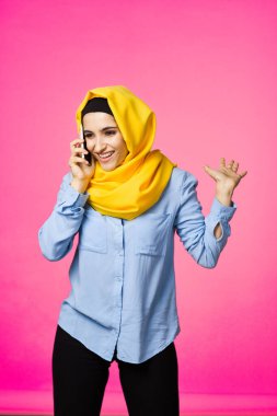 Sarı tesettürlü müslüman kadın telefon teknolojisi pembe arka planda konuşuyor.