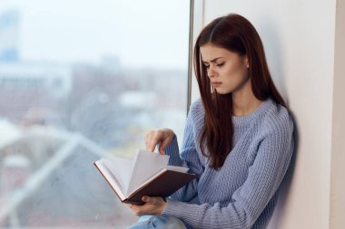 Kadın pencerenin yanında kitap okuyor, bir bardak içkiyle dinleniyor.