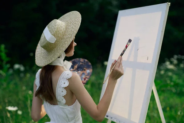 Mujer en vestido blanco pinta un cuadro sobre caballete de la naturaleza —  Fotos de Stock