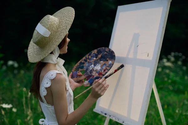 Mujer en vestido blanco pinta un cuadro sobre caballete de la naturaleza —  Fotos de Stock