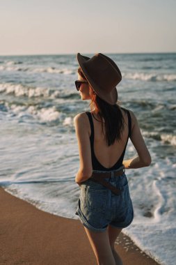 Kumsalda yürüyen bir kadın, tatil güneşinde seyahat ediyor.