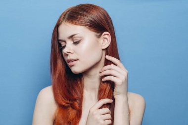 Çıplak omuzlu bir kadın. Kızıl saçlı, mavi arkaplan.