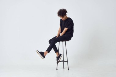 Sandalyede oturan kıvırcık adam moda arkaplanı pozu veriyor.