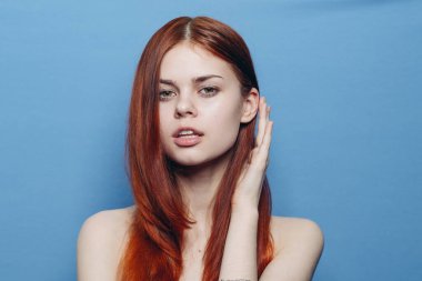 Çıplak omuzlu çekici bir kadın. Kızıl, yakın plan, mavi arka plan.