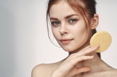 Ellerinde süngerle çıplak omuzlarıyla cilt bakımı yapan bir kadın.