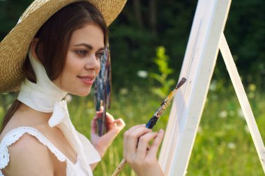 Bir palet boyalı kadın açık havada bir resim çiziyor.