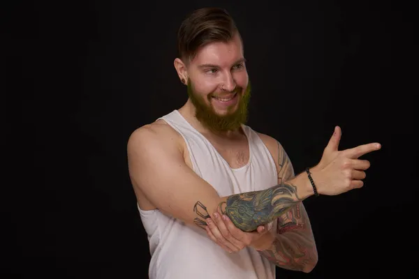 Uomo barbuto con tatuaggi sulle braccia gesticolando con le mani sfondo scuro — Foto Stock
