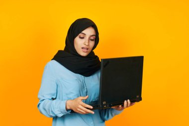 Elinde dizüstü bilgisayarla siyah tesettürlü bir kadın. Duygularını stüdyo yaşam tarzına yansıtıyor.