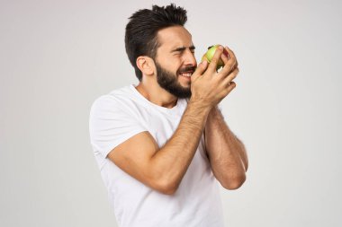 Beyaz tişörtlü sakallı bir adam sağlıklı yiyecekler tutuyor.