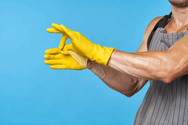 Man in apron with pumped up body rubber gloves cleaning blue background — Stock Photo, Image