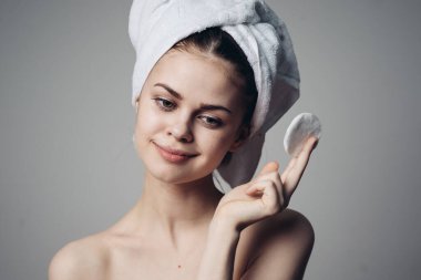 Ellerinde pamuk pedlerle, duştan sonra çıplak omuzlarını temizleyen bir kadın.