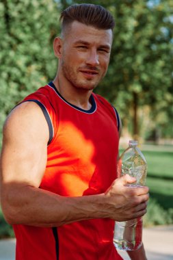 Parkın içinde elinde dambıllar olan atletik bir adam.