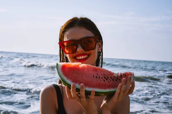 Cheerful woman in black swimsuit eating watermelon on the beach — Stock Photo, Image