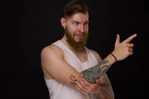 Бородатый мужчина с татуировками на руках жестикулирует руками на тёмном фоне — стоковое фото