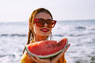 Okyanus kıyısındaki sahilde karpuz yiyen bir kadın.
