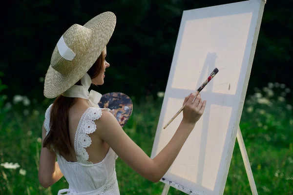 白いドレスの女性は自然のイーゼルに絵を描く — ストック写真