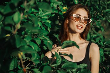 Gülümseyen kadın güneş gözlüğü takıyor yeşil yapraklar doğal moda.