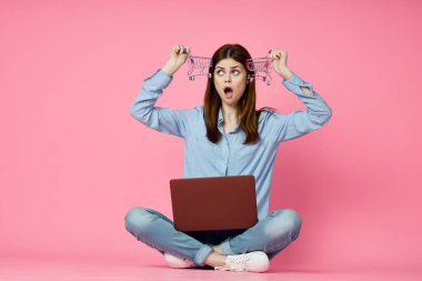 Dizüstü bilgisayarı olan bir kadın internet iletişiminde pembe arka planda oturuyor.