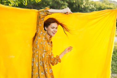 Sarı elbiseli gülümseyen kadın doğaya sarılık pozu veriyor.