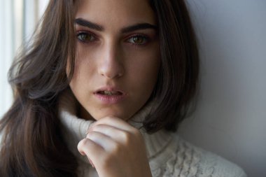 Pencerenin yanında beyaz kazaklı güzel bir kadın var.