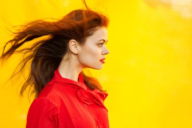 Kırmızı elbiseli güzel bir kadın sarı fona yakın poz veriyor.