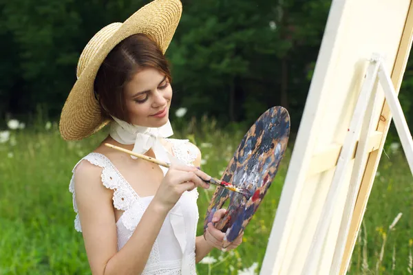 Pretty woman in hat artist paints a picture on nature paint — Stock Photo, Image