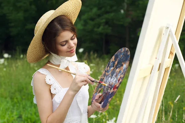 Mooie vrouw in hoed kunstenaar schildert een beeld op de natuur verf — Stockfoto