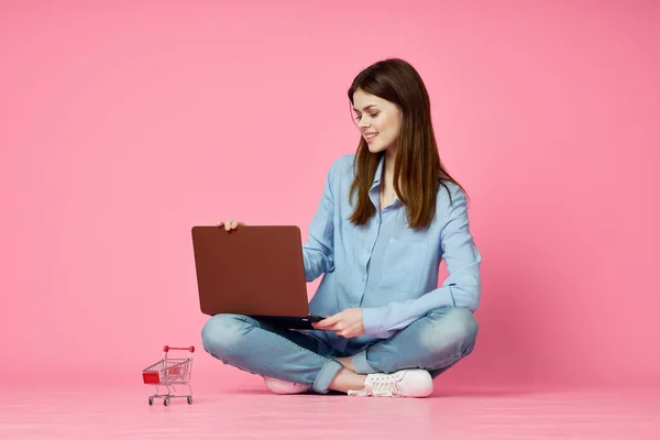 Mujer con el ordenador portátil sentado en el suelo internet comunicación en línea rosa fondo — Foto de Stock