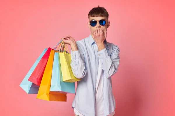 Kille i solglasögon med shoppingväskor rosa bakgrund — Stockfoto