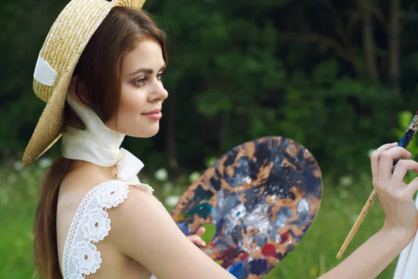 Ładna kobieta w kapeluszu artysta maluje obraz na farbie natury — Zdjęcie stockowe