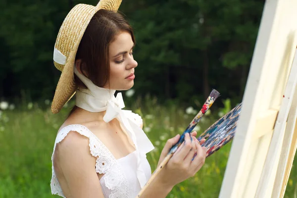 Bonita mujer en sombrero artista pinta un cuadro en la pintura de la naturaleza —  Fotos de Stock