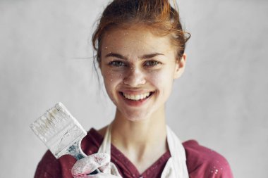 Beyaz önlüklü kadın ressam elinde fırçayla eğleniyor.