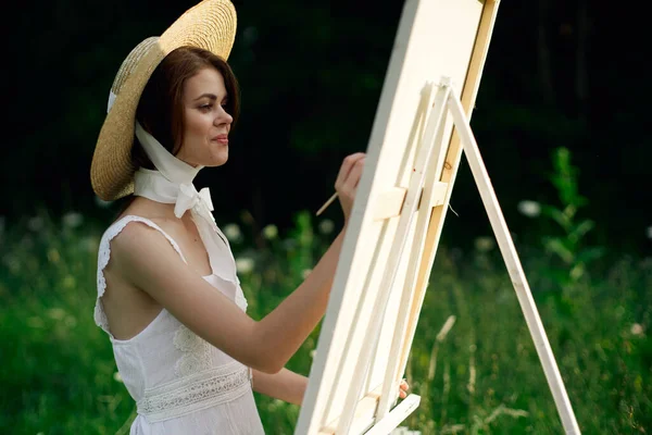 Жінка в білому платті малює картину на мольберті природи — стокове фото