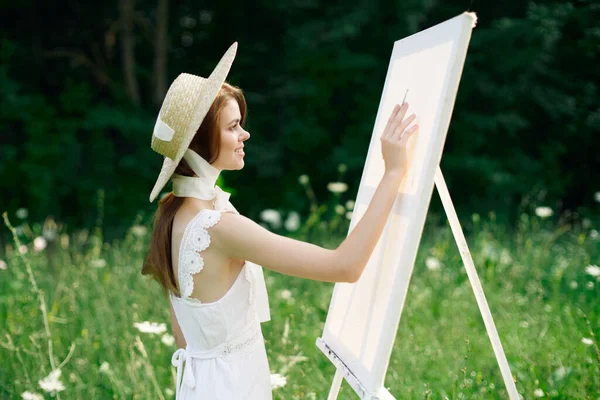 Mulher de vestido branco na natureza pinta um quadro de um hobby de paisagem — Fotografia de Stock
