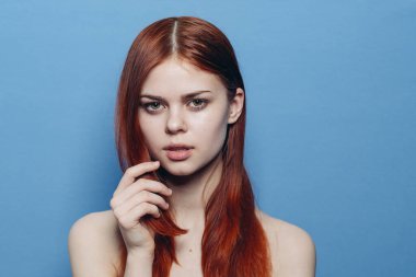 Çıplak omuzlu bir kadın. Kızıl saçlı, mavi arkaplan.