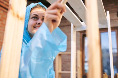 Koruyucu takım elbiseli neşeli kadın boyacı evini tamir ediyor.