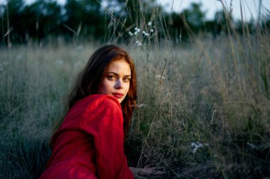 Tarladaki kadın kırmızı elbiseli çimenlerin üzerinde yatıyor.