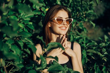Gülümseyen kadın güneş gözlüğü takıyor yeşil yapraklar doğal moda.