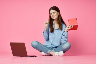 Dizüstü bilgisayar alışverişi yapan pembe arka planda oturan bir kadın.
