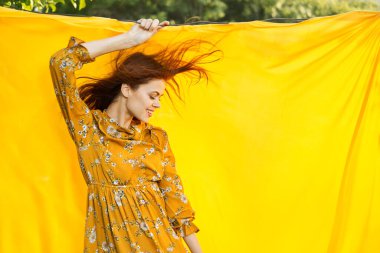 Sarı elbiseli gülümseyen kadın doğaya sarılık pozu veriyor.