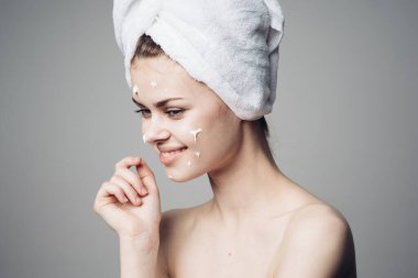 Çıplak omuzlu kadın yüz kremi sürmüş.