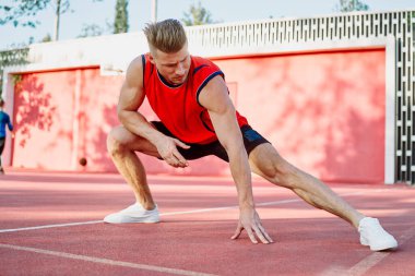 Spor salonunda spor yapan kırmızı tişörtlü bir adam egzersiz yapıyor.