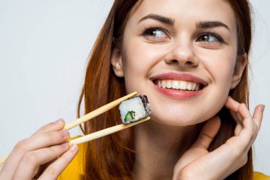 Japon yemek çubuklarıyla suşi yiyen kadın arka planda ışık yayıyor.